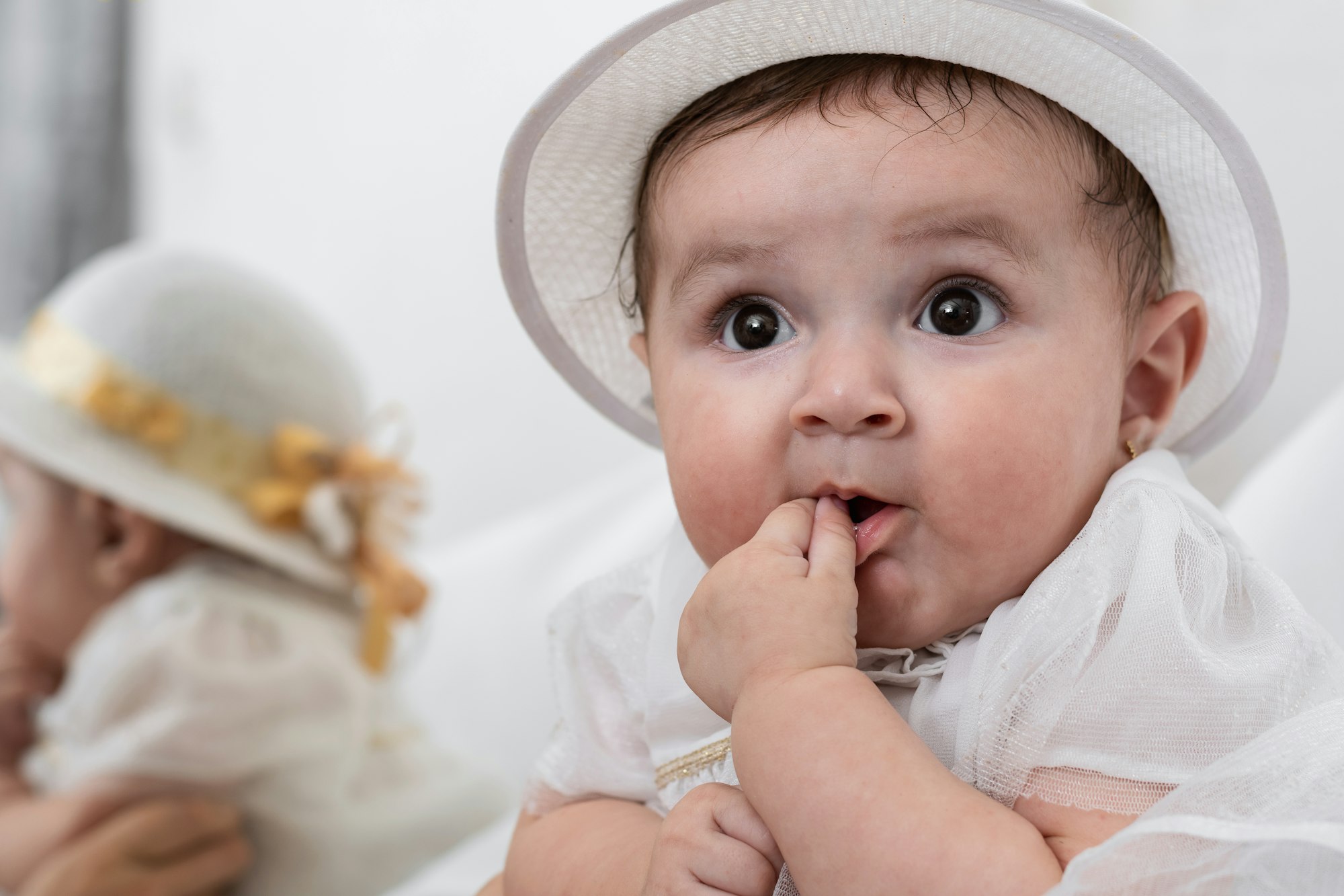 a beautiful white-skinned latina baby girl with a white dress and hat, looking with curiosity